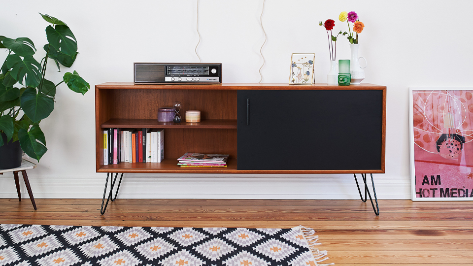 Ein Vintage Sideboard steht zwischen einer Zimmerpflanze und einem gerahmten Kunstdruck.