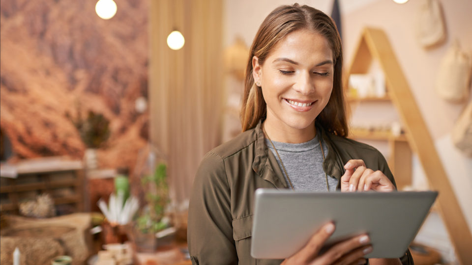 Die Geschäftsführerin eines Concept Stores blickt erfreut auf den Bildschirm ihres Tablets.