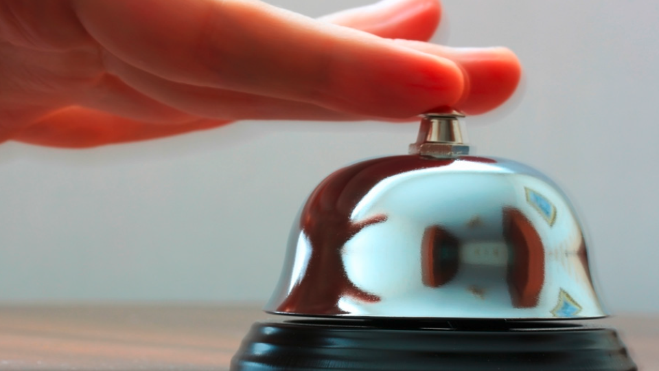 Close-up of a hand ringing a bell on a desk