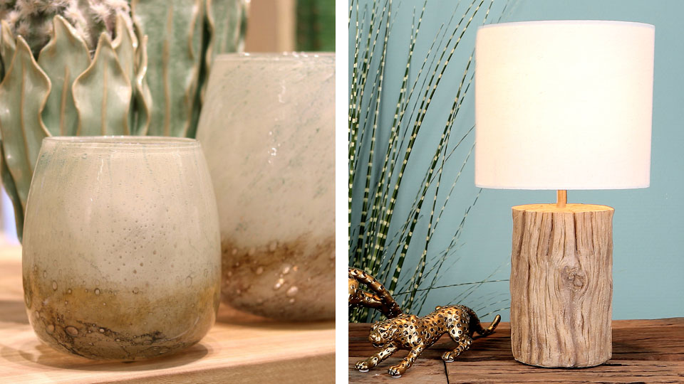 Conzoom Solutions Sommer Trend Shishi Kaefer GoldWindlichter aus grau beschichtetem Glas stehen vor einer floralen Keramik. Ein Jaguar aus Messing steht neben einer Tischlampe mit Holzblockbasis.
