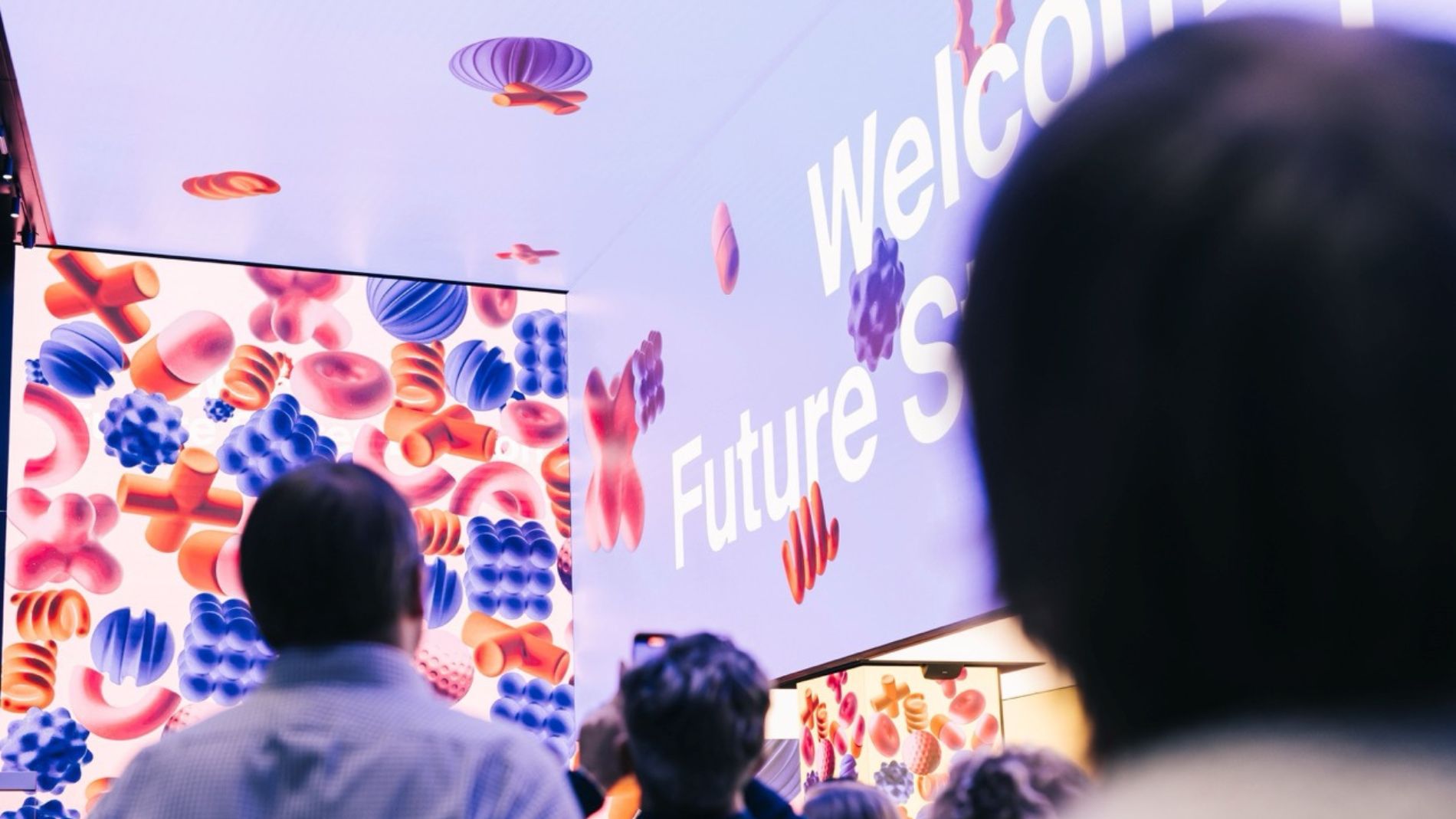 Visitors at a trade fair standing in front of a large LED wall reading “Welcome Future Shopping”.