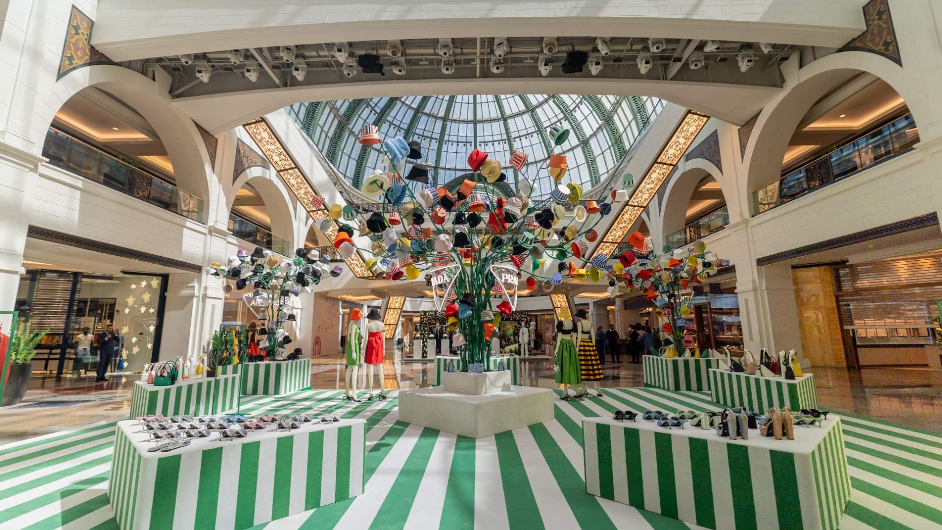 Creative product display in a shopping mall featuring green and white striped stands and floating decorations beneath a glass dome.