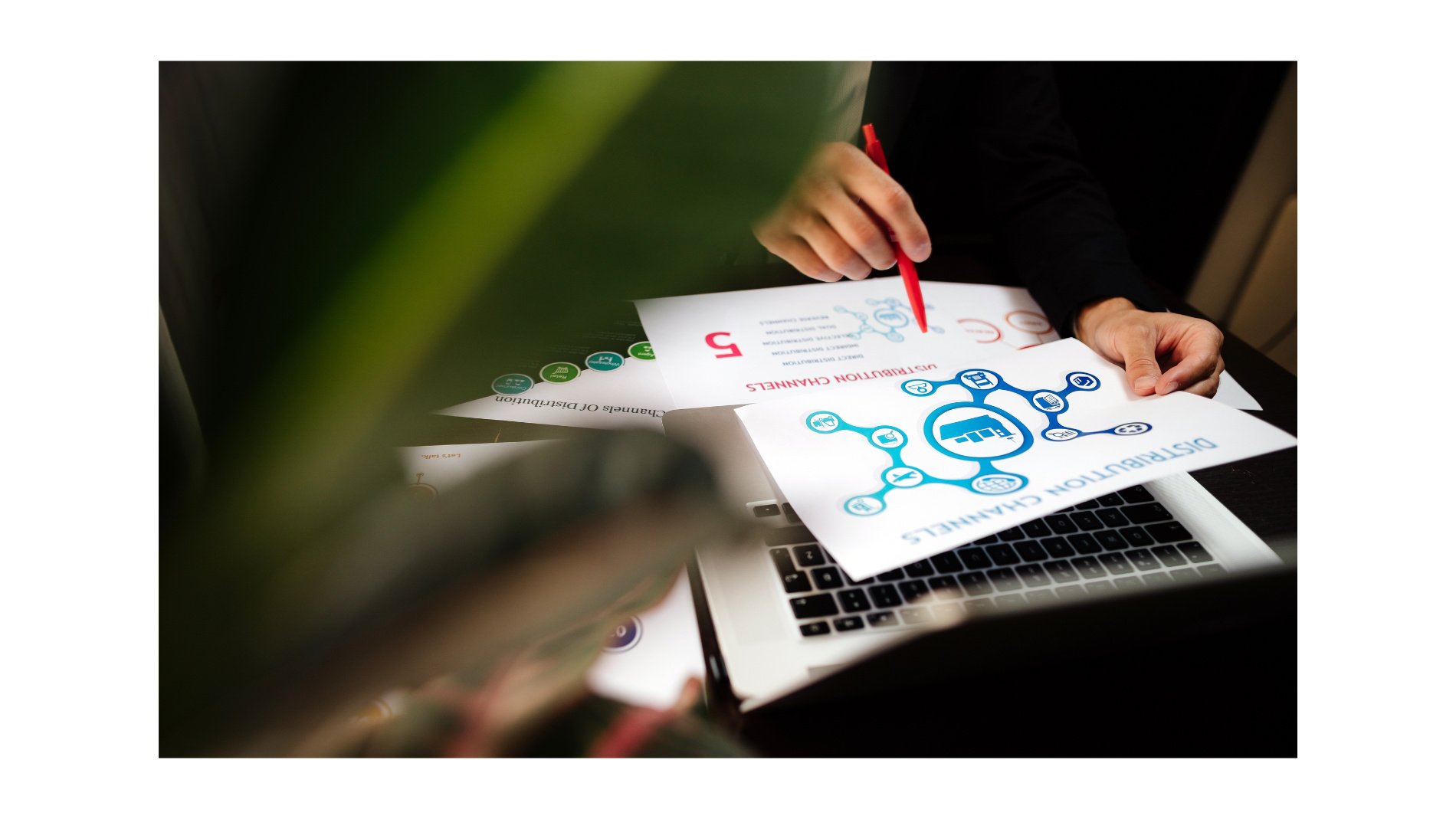 Person points with pen to documents next to a laptop