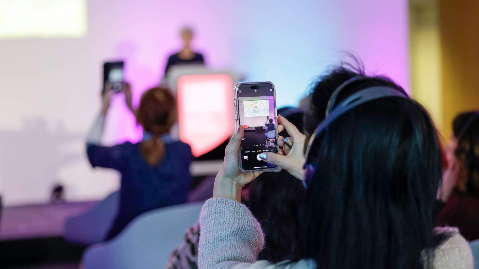 Woman takes a photo of a speaker on stage with her mobile phone